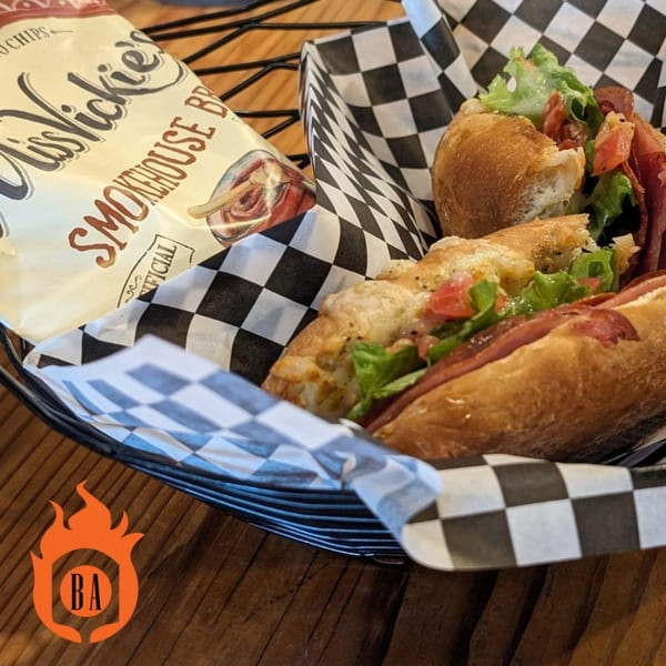 A sub sandwich with lettuce, tomato, and meat, next to a bag of Miss Vickie's chips.