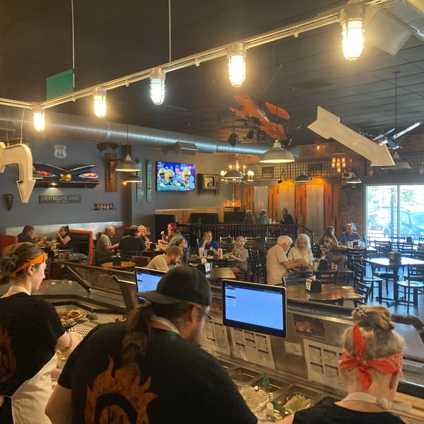 Back Alley Pizza's lively dining room with customers eating and staff working behind the counter.