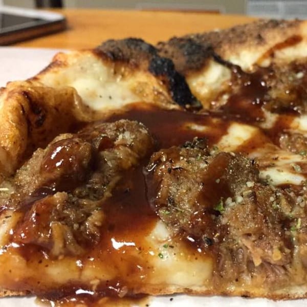 Close-up of a slice of Back Alley Pizza with BBQ sauce, pulled pork, and cheese.